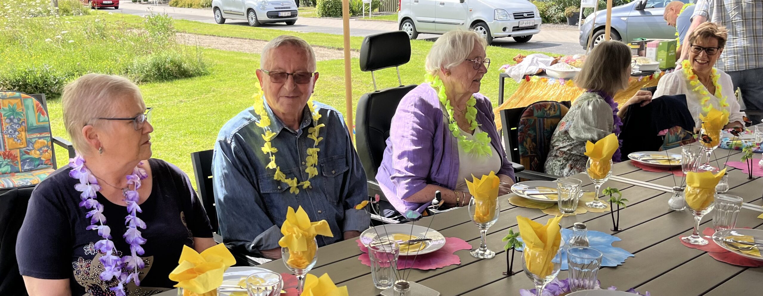 Beboerne i boligafdelingen Trianglen sidder med Hawaii-inspirerede blomsterkæder om halsen ved det smukt pyntede bord.